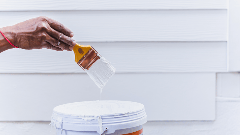 Maalari kastaa pensselin maaliämpäriin